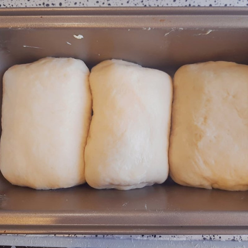 Ba khối bột bánh mì sữa Nhật Bản đã được tạo hình và xếp gọn gàng trong khuôn, chuẩn bị cho lần ủ cuối cùng.