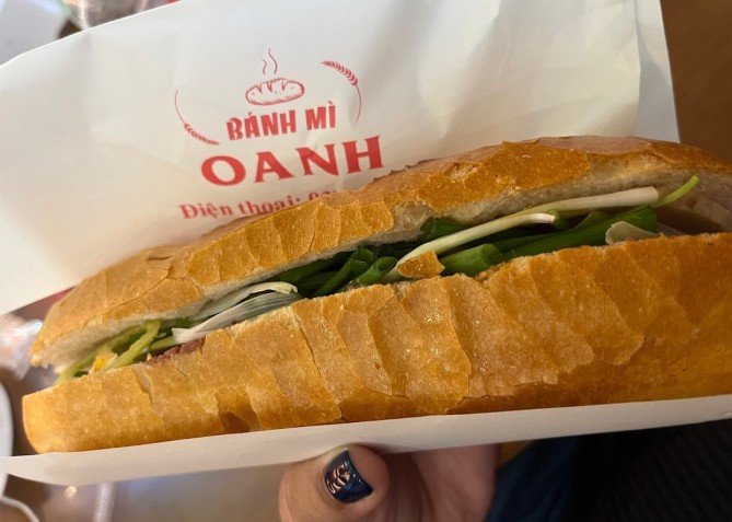 Bánh mì Oanh Lê Thánh Tôn được xẻ đôi, hé lộ nhân thịt nguội, pate và rau thơm tươi xanh.