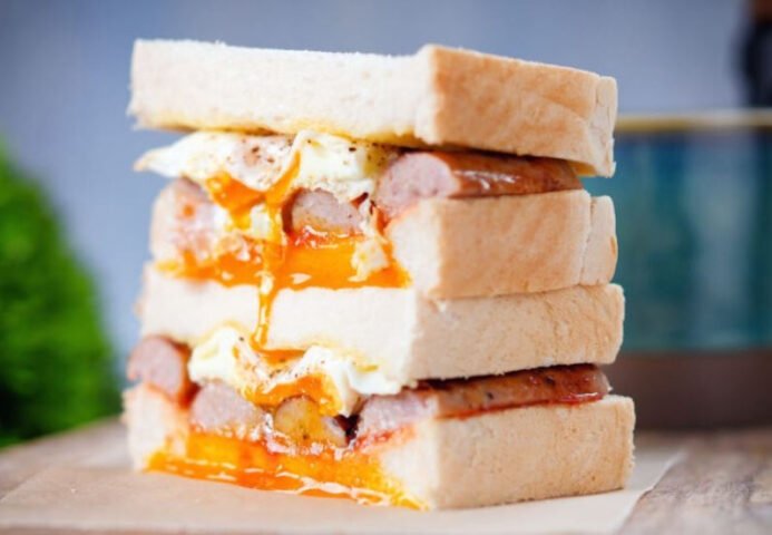 Bánh mì sandwich kẹp xúc xích với trứng ốp la và rau tươi, chuẩn bị cho bữa sáng