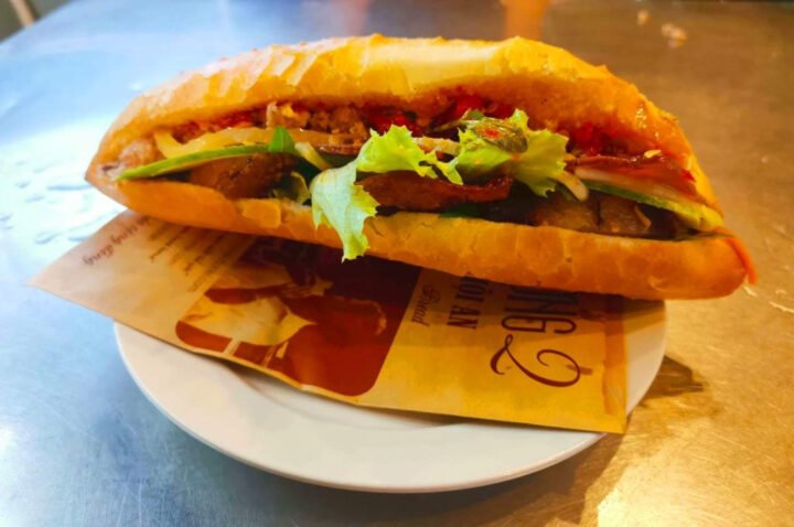 Bánh mì thập cẩm Phượng, biểu tượng ẩm thực Hội An, đầy ắp thịt, pa-tê và rau xà lách trên đĩa trắng ở quán ăn đường phố.
