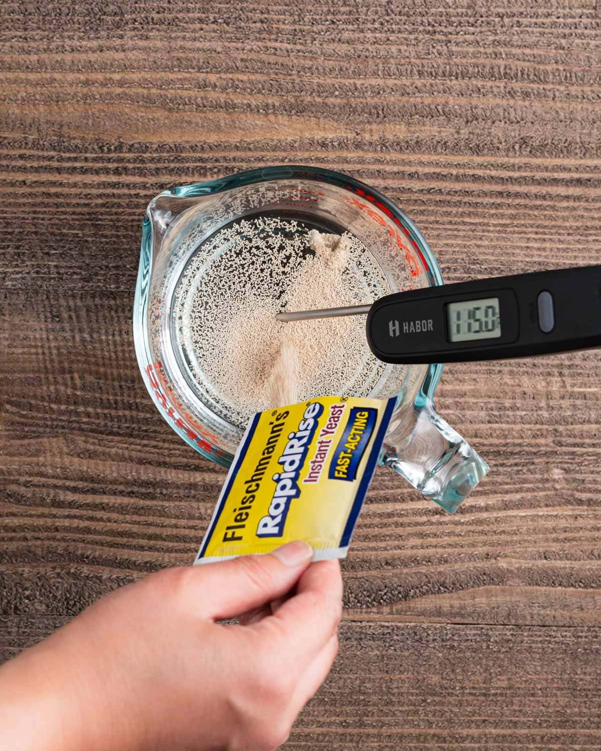 Đổ men vào nước ấm trong cốc đong với nhiệt kế kỹ thuật số hiển thị 115°F.