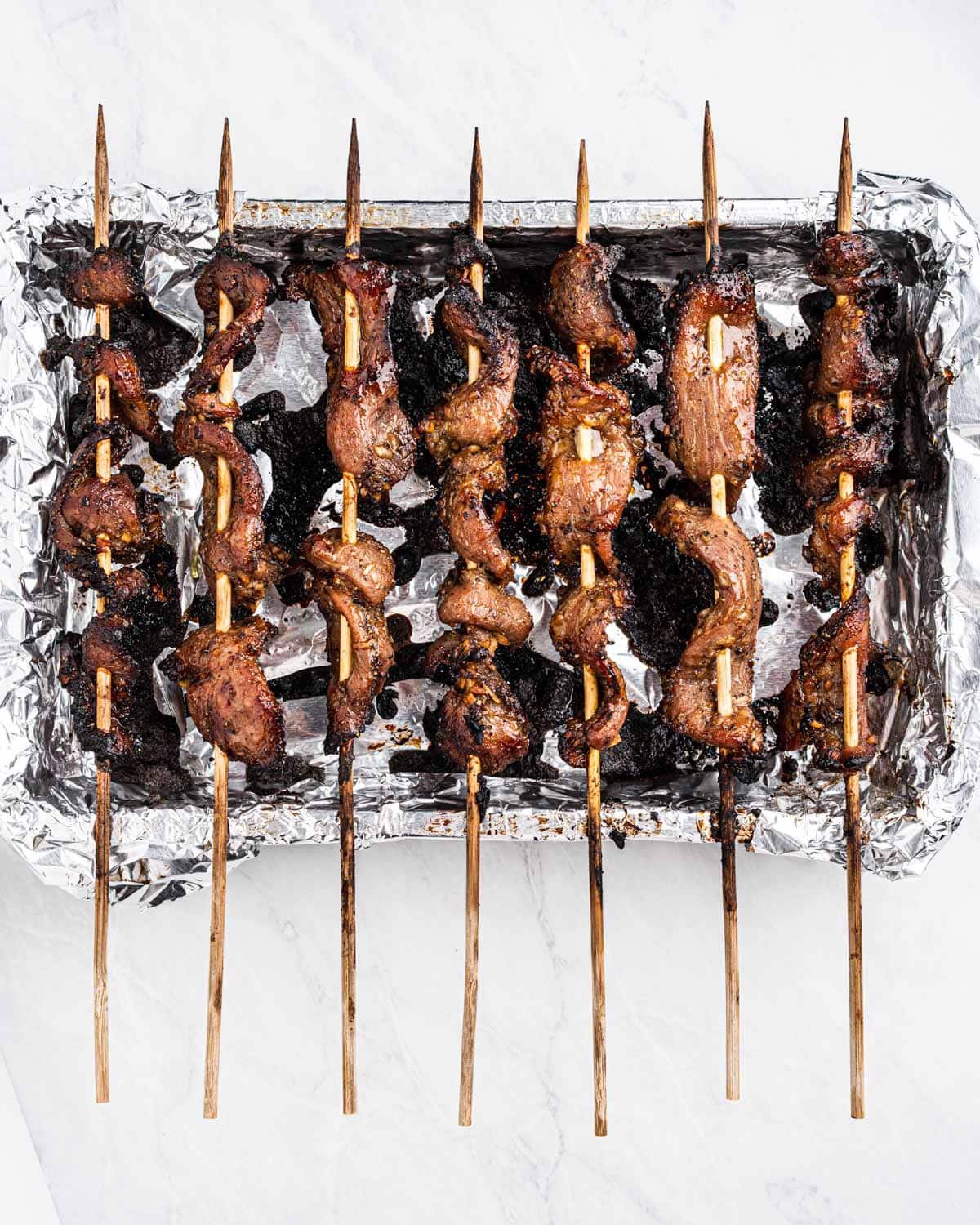 Freshly grilled pork on skewers resting on top of a baking tray.