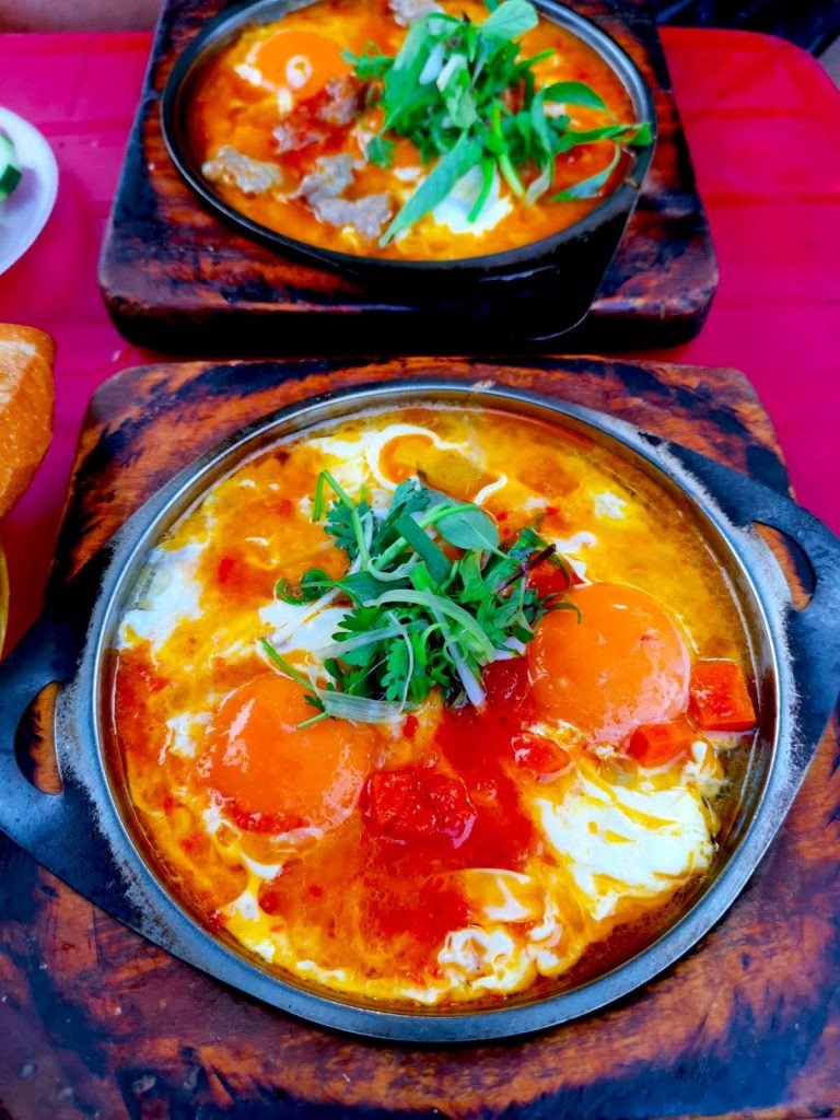 Hai đĩa kim loại đầy trứng ốp la, cà chua và rau xanh trên khay gỗ tại quán ăn đường phố Op La Dong Hoi An.