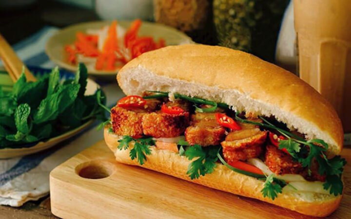 Hình ảnh ổ bánh mì heo quay với rau thơm và nước sốt đặc trưng, sẵn sàng cho bữa sáng ngon miệng