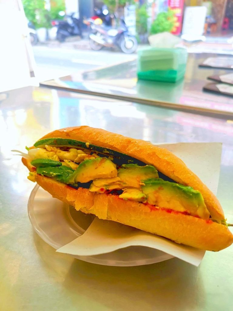 Một lát bánh mì kẹp bơ, một trong những chiếc bánh mì chay ngon nhất Hội An, trên bàn kim loại tại Phi Bánh Mì.