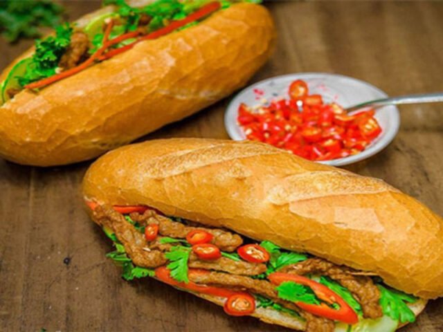 Một người phụ nữ đang chuẩn bị bánh mì chả cá tại quầy bán hàng, thể hiện quy trình làm ra những ổ bánh mì nóng hổi và hấp dẫn.