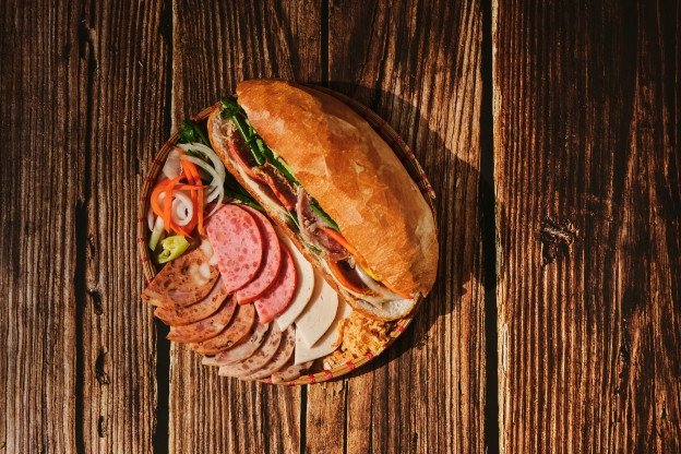 Một ổ bánh mì Huỳnh Hoa thơm ngon, vàng giòn được kẹp đầy đủ nhân và rau củ tươi, thể hiện độ lớn và hấp dẫn của món ăn