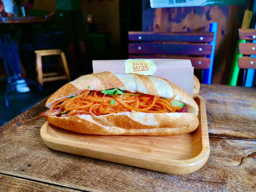 Một ổ bánh mì Việt Nam trên khay gỗ đầy rau và cà rốt màu cam tươi sáng tại Bánh Mì 25 Hà Nội.