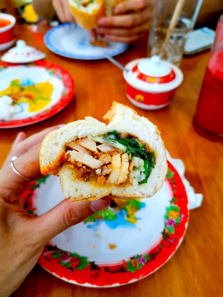 Một phụ nữ cầm chiếc bánh mì Việt Nam cắt đôi, bên trong đầy thịt và xà lách, tại The Banh Mi Queen ở Hội An.
