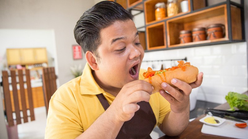 Người đang ăn bánh mì xúc xích, thể hiện tầm quan trọng của việc kiểm soát khẩu phần để tránh tăng cân.