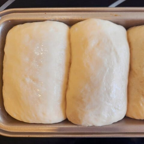 Người làm bánh đang nhồi bột bánh mì sữa Nhật Bản bằng tay trên mặt bàn, phát triển độ đàn hồi của bột.