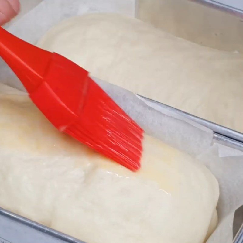 Phết hỗn hợp trứng sữa lên mặt bánh mì nhân chà bông trước khi nướng