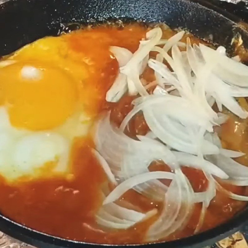 Rắc hành tây và gia vị vào chảo cá hộp trứng ốp la