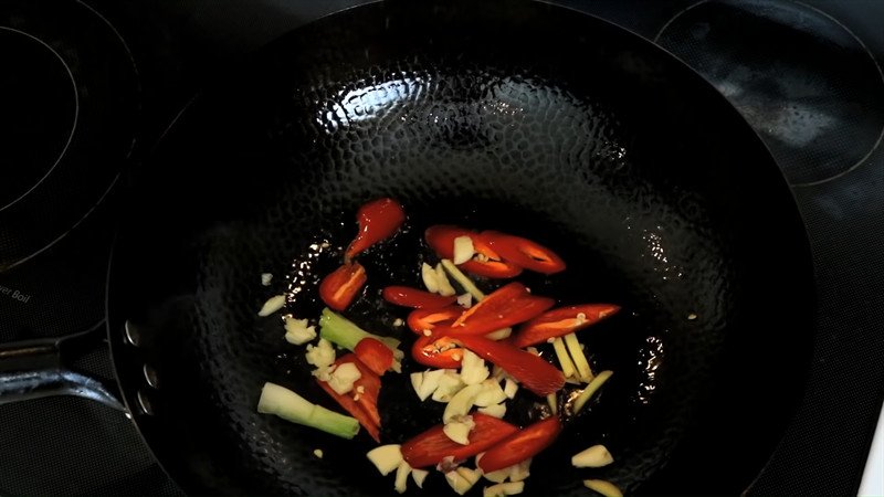 Chảo đang phi thơm tỏi, ớt, gừng và đầu hành trên bếp với lửa vừa, tạo hương thơm hấp dẫn.
