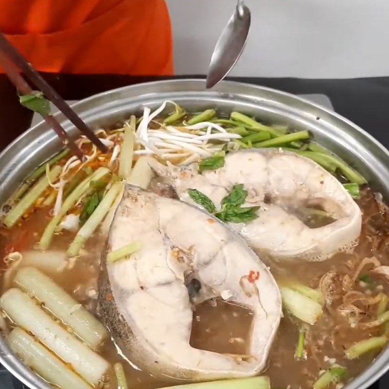 Cho cá bớp và tỏi sả phi vào nồi lẩu cá bớp măng chua đang sôi