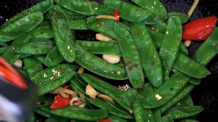 Đĩa lạp xưởng đã xào sơ vàng ươm, đặt cạnh đậu Hà Lan xanh tươi trong chén sẵn sàng chế biến.