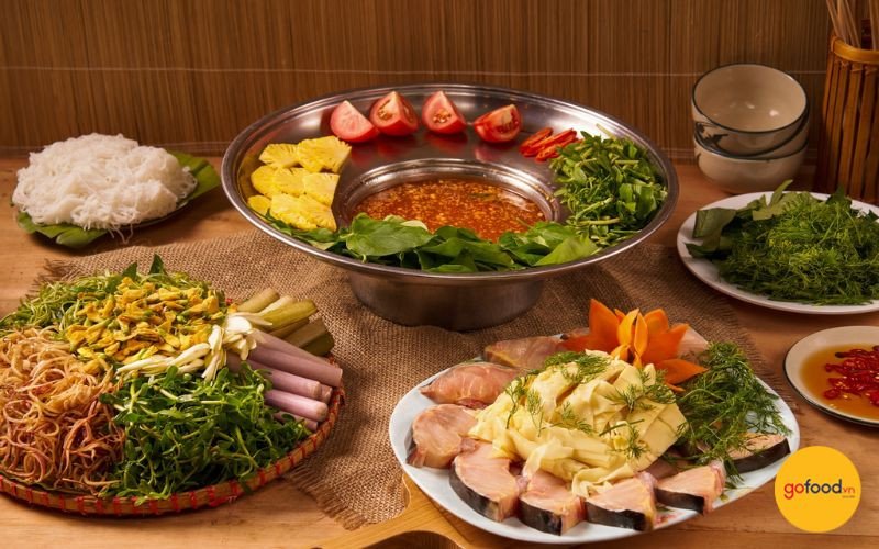 Mâm lẩu cá tầm thập cẩm đầy đủ rau, nấm và bún tươi cho bữa ăn gia đình ấm cúng