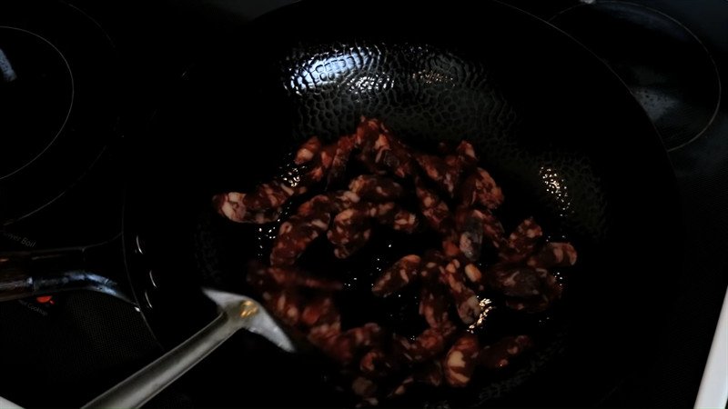 Món đậu Hà Lan xào lạp xưởng đang được đảo đều trong chảo, các nguyên liệu hòa quyện cùng gia vị.