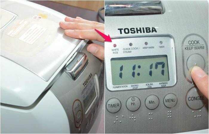 Một bàn tay đang nhấn nút khởi động trên bảng điều khiển của nồi cơm điện tử Toshiba