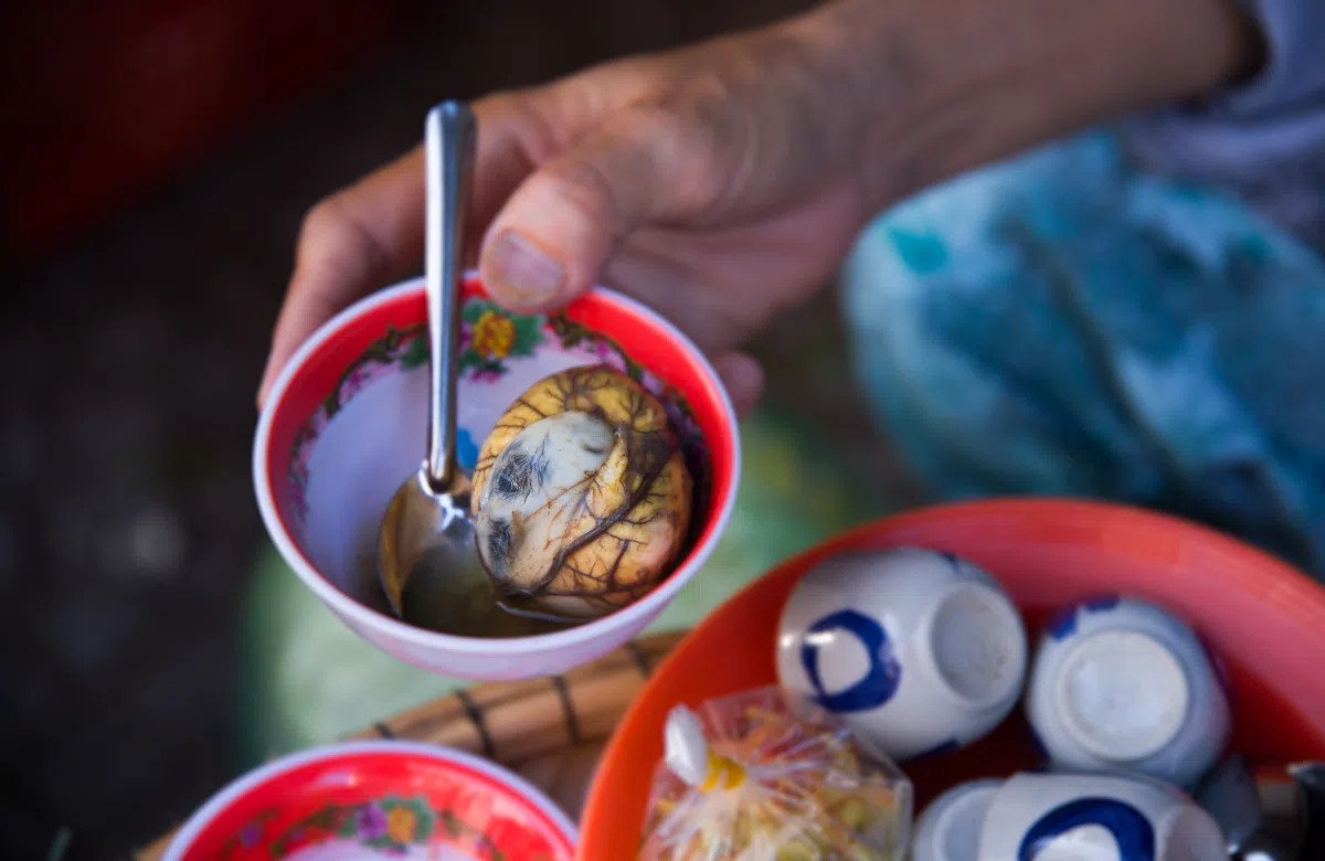 Một nhóm bạn đang thưởng thức món trứng hột vịt lộn nóng hổi với rau răm và gia vị.