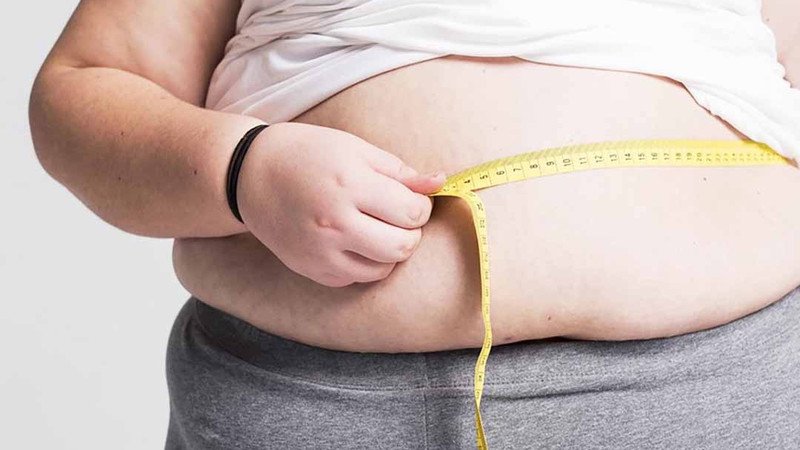 Một phụ nữ đang kiểm tra cân nặng của mình, hình ảnh liên quan đến vấn đề béo phì