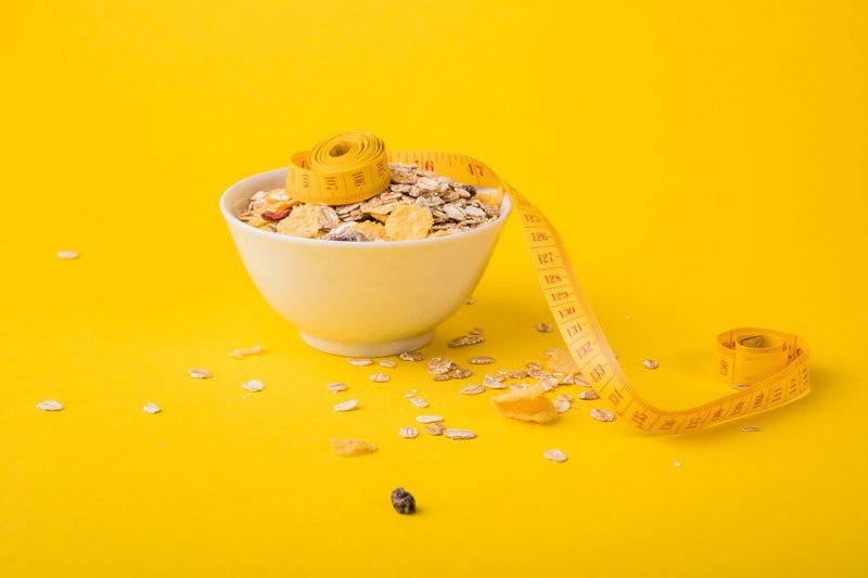 Một phụ nữ đang mỉm cười và thưởng thức bát yến mạch buổi sáng với hoa quả, tượng trưng cho lối sống lành mạnh và giảm cân