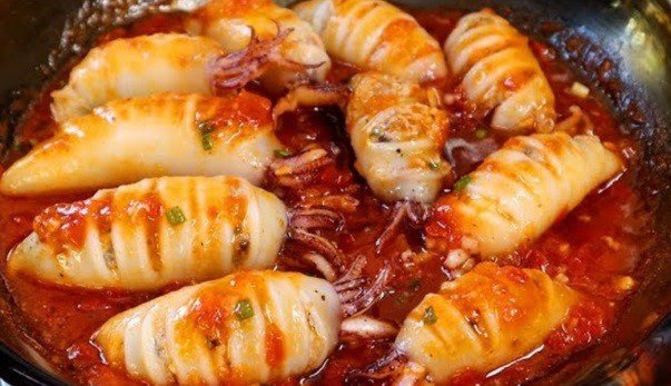 Mực nhồi thịt đang được sốt cùng cà chua trong chảo, tạo nên hương vị hòa quyện