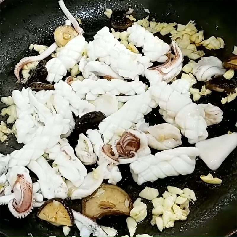 Mực và các loại rau củ đang được xào nhanh trên chảo lớn, tạo nên hương thơm hấp dẫn