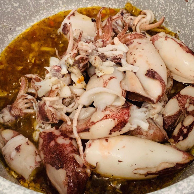 Mực và nước sốt sa tế đang được đảo đều trên chảo, tạo nên hương thơm đặc trưng của món ăn.