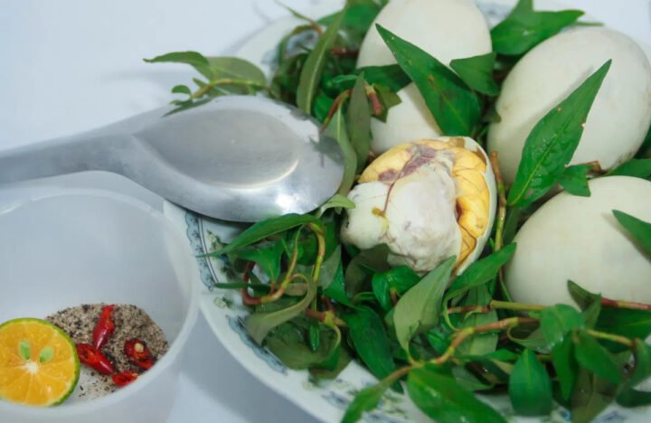 Người đang cầm một quả trứng hột vịt lộn đã bóc vỏ, cho thấy phần lòng đỏ và phôi bên trong.