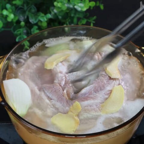 Người đầu bếp sơ chế miếng thịt ba chỉ quay tươi sống bằng cách rửa sạch và cạo da