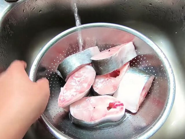 Người phụ nữ đang sơ chế cá ba sa trên thớt, chuẩn bị cho món kho