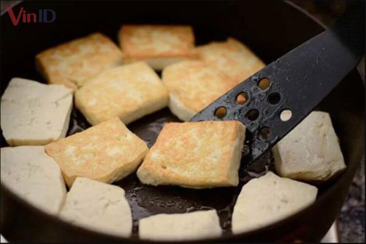 Những miếng đậu hũ vàng ruộm được chiên đều các mặt trên chảo dầu, sẵn sàng cho món canh cà tím chay thơm ngon