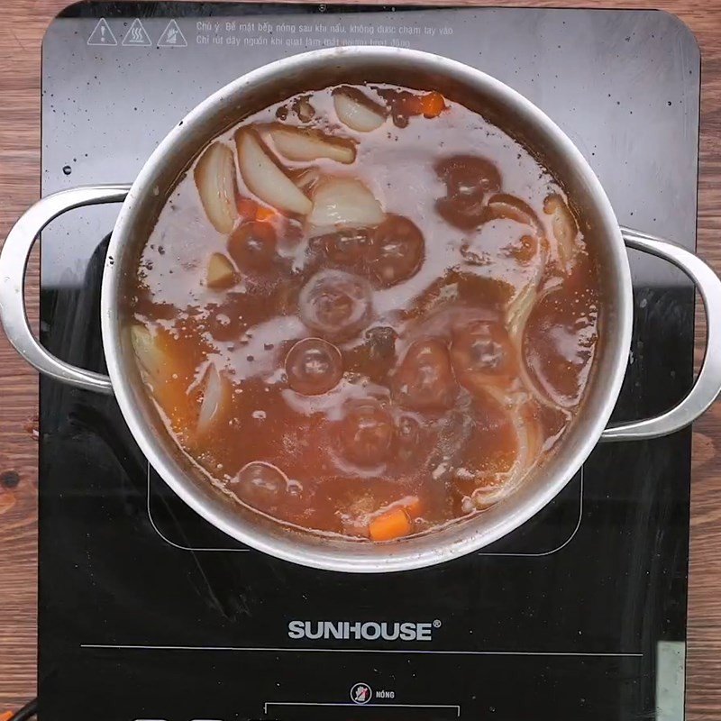 Nồi bò sốt vang đang sôi nhẹ trên bếp, thịt bò và rau củ mềm nhừ