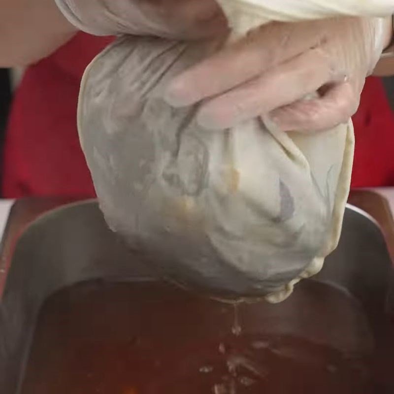 Nước cốt trà bí đao nóng đang được lọc qua rây, với các nguyên liệu đã nấu bên trong