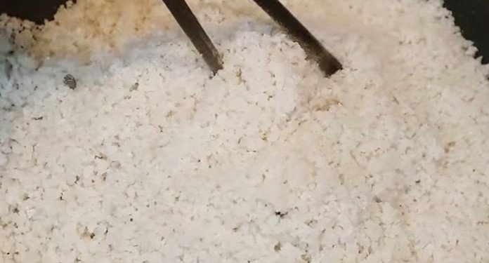 Rang muối hạt trên chảo nóng để loại bỏ độ ẩm, chuẩn bị làm thịt heo muối khô.