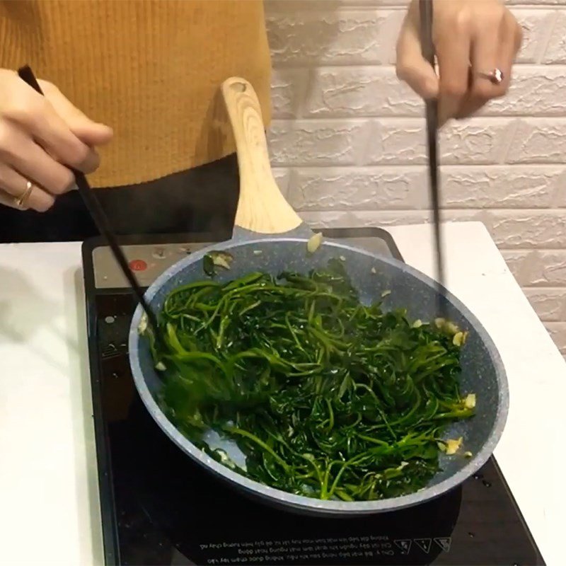 Rau khoai lang đang được xào nhanh trong chảo trên lửa lớn