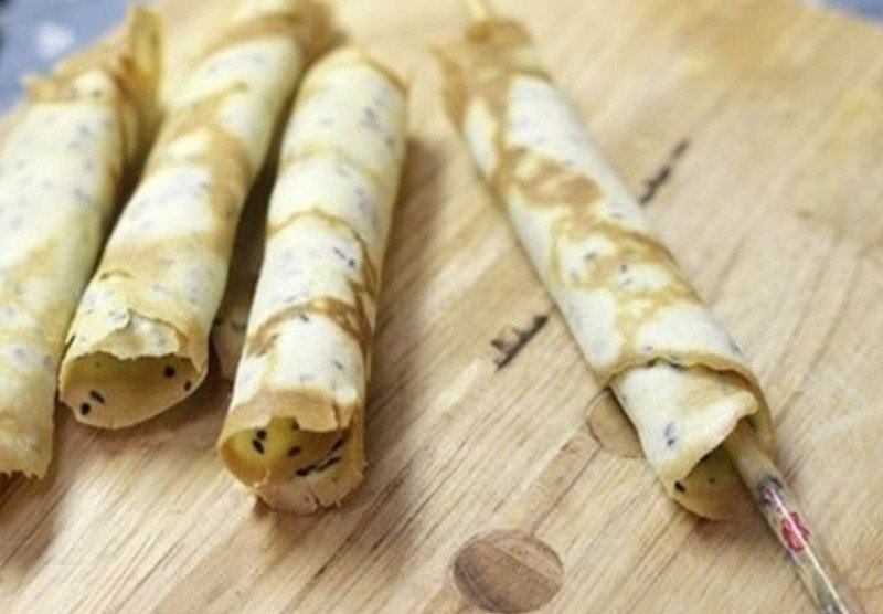 Thao tác cuốn bánh kẹp còn nóng hổi thành hình ống dài trong quá trình học cách làm bánh kẹp cuốn.