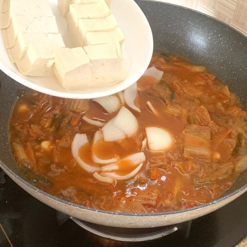 Thêm hành tây và đậu hũ vào canh kim chi thịt bò đang sôi